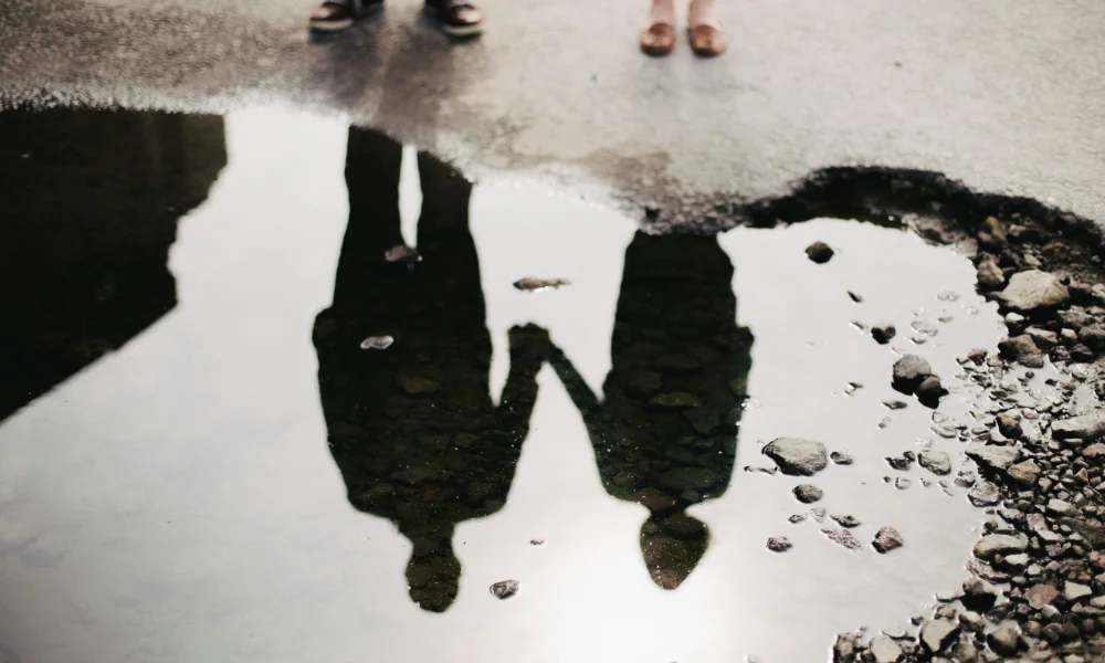 A man and a women holding hands, their reflection in the water.